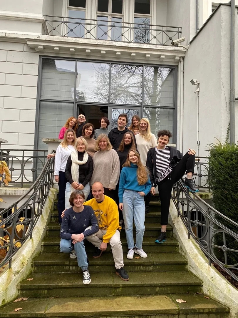 Eine Wissenschaftlerin und ein Wissenschaftler arbeiten hinter einer Glasfassade und mischen Chemikalien mit Großgeräten.